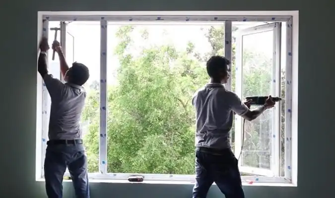 Two technicians installing large white aluminum impact window indoors