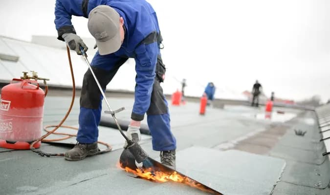 Roofer torch-applying modified bitumen membrane on flat commercial roof