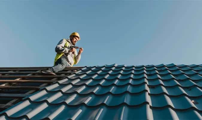 Roofer installing dark teal metal tile roof on South Florida home