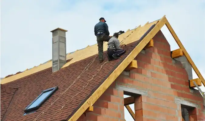 Two roofers installing shingles on residential home under construction