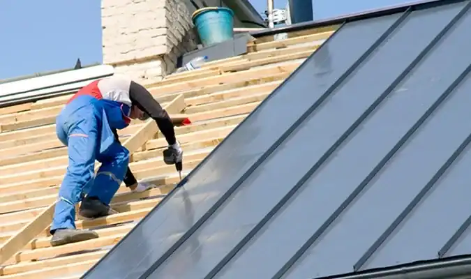 Contractor installing metal standing seam roof panels on residential home