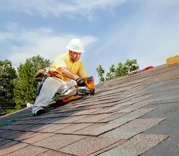 Roofer installing asphalt shingles with nail gun on residential roof