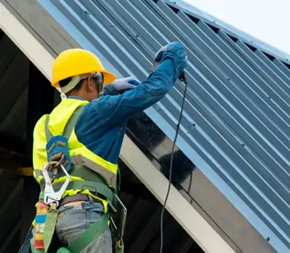 Roofer in safety harness installing metal roof panels South Florida