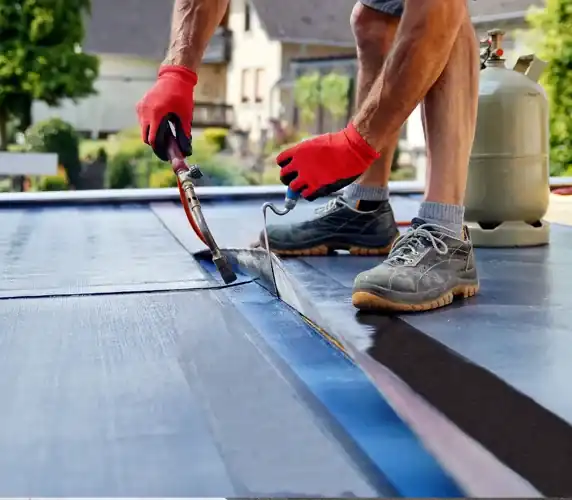Roofer torch-welding modified bitumen membrane on flat roof