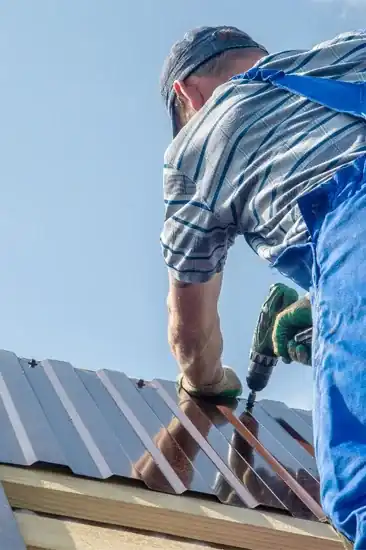 Roofer installing metal roof panels with power drill on sunny day