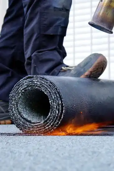 Roofer torch-applying modified bitumen membrane for flat roof