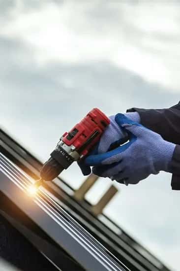 Gloved roofer drilling metal roofing panel during installation South Florida