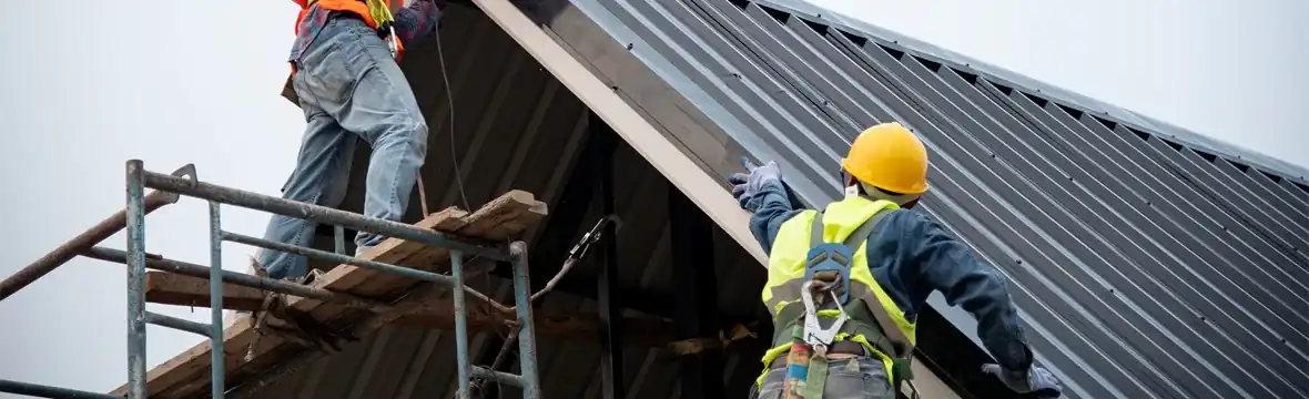 Two roofers installing metal roof panels on pitched roof with scaffolding