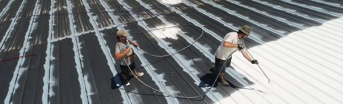Two roofers applying reflective coating to corrugated metal roof