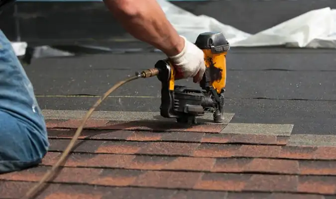 Roofer nailing asphalt shingles with pneumatic nail gun
