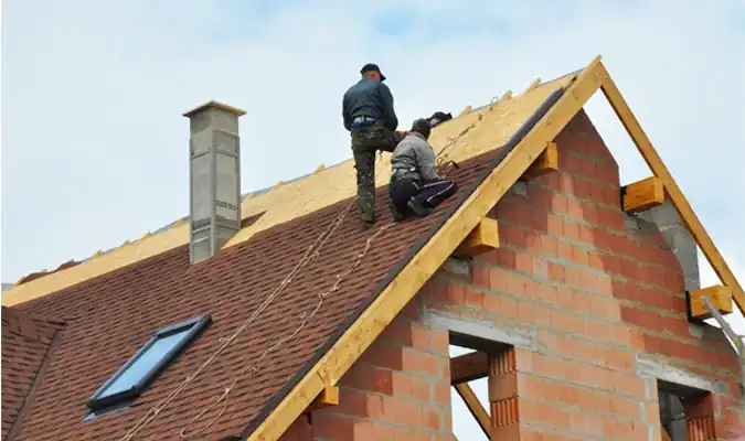 Two roofers installing shingles on residential home under construction