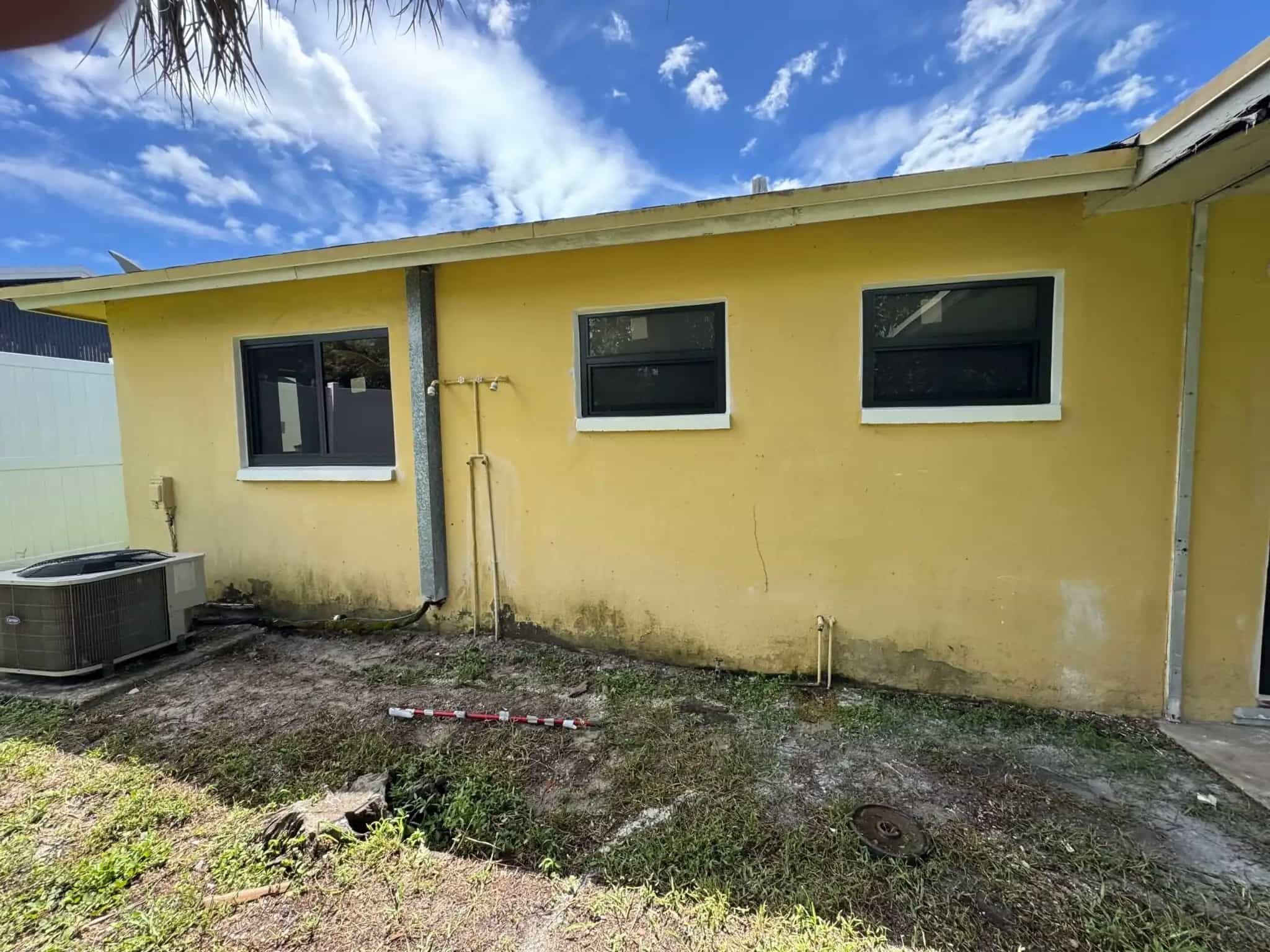New dark-frame impact windows installed on yellow stucco home exterior