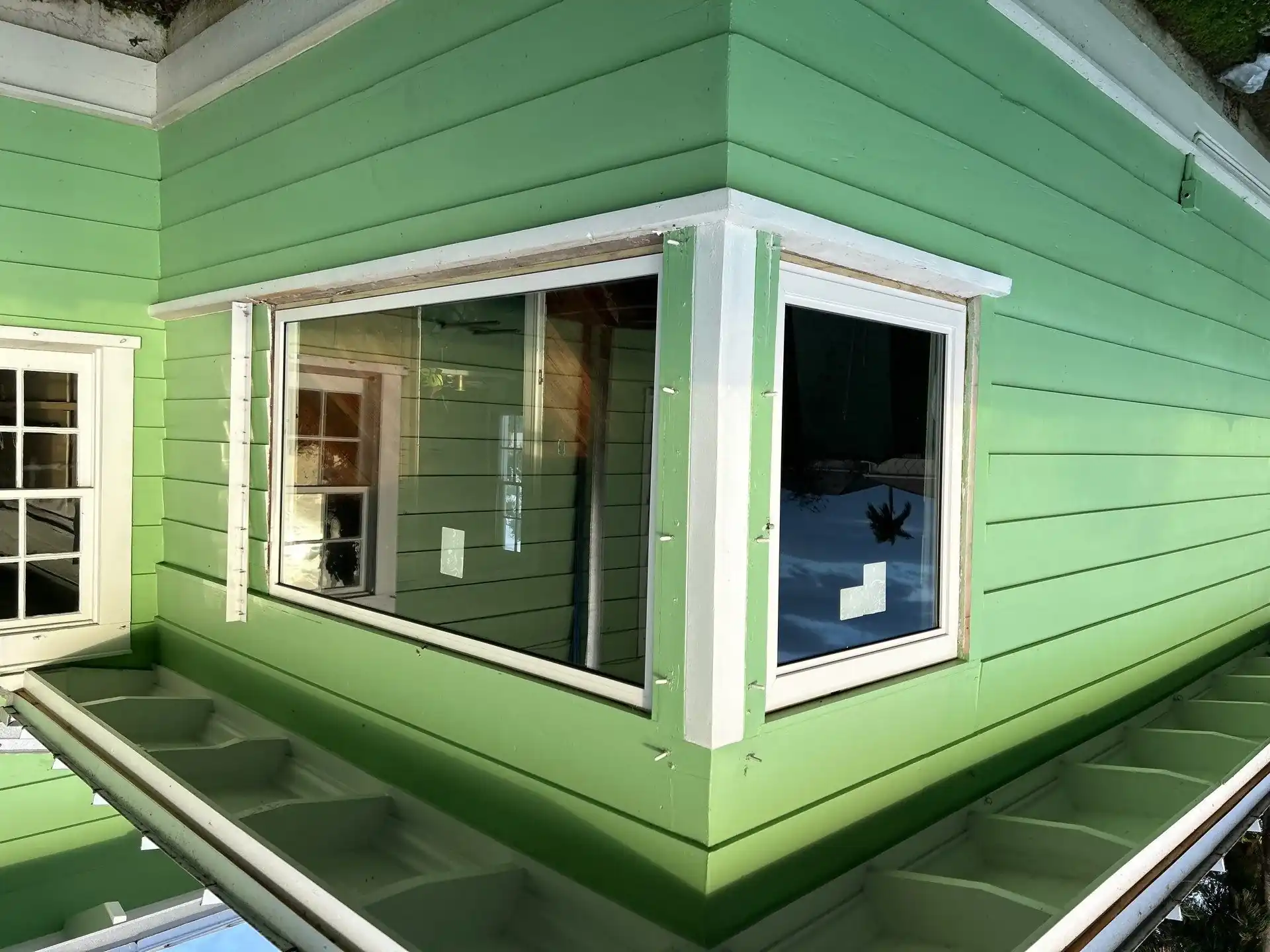 Corner impact windows installed on green wood-sided Homestead home