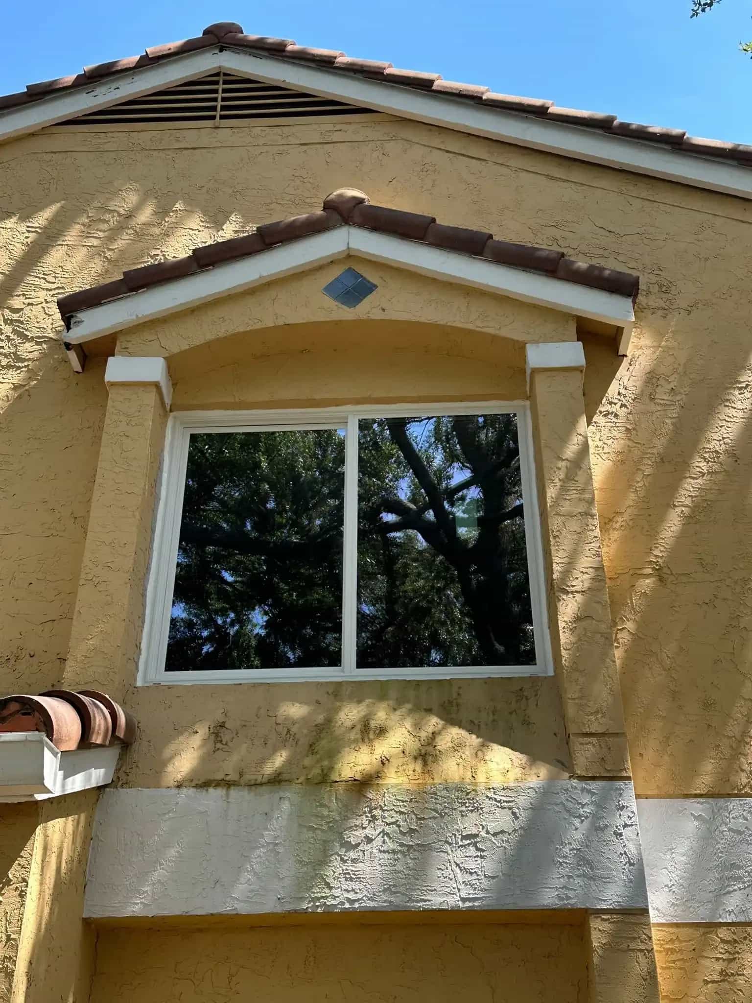 Impact sliding window installed on yellow stucco home gable Oakland Park FL