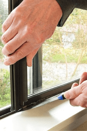 Technician sealing dark-framed impact window frame during installation