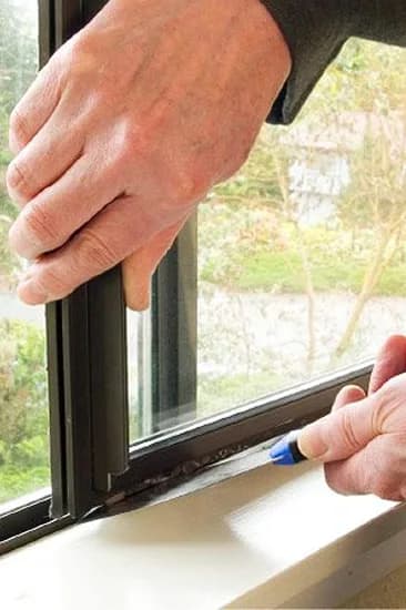 Technician inspecting dark-framed impact window during installation